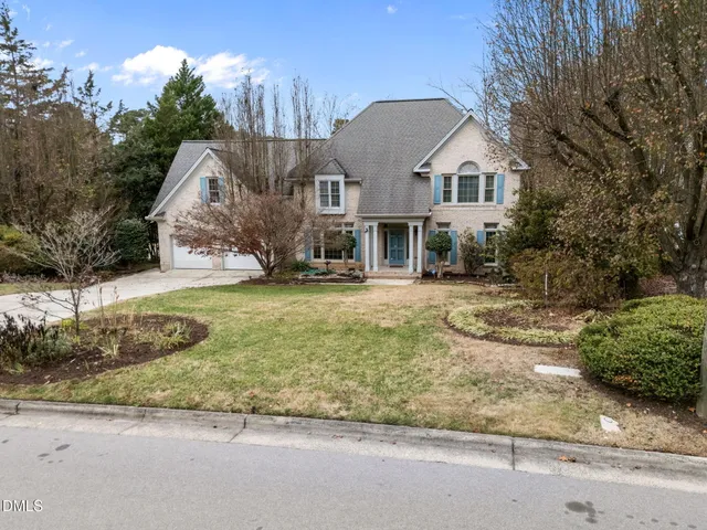 a view of a white house with a yard plants and large tree