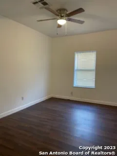 an empty room with wooden floor chandelier fan and windows