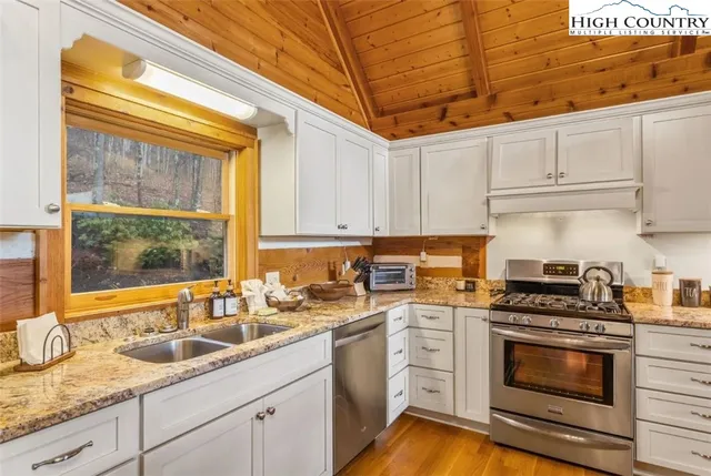 a kitchen with granite countertop stainless steel appliances a sink window and cabinets
