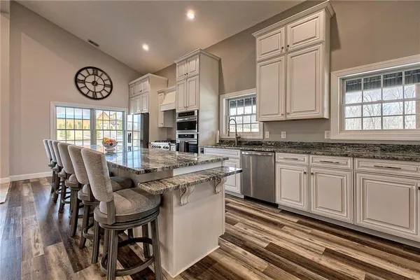 a open kitchen with stainless steel appliances granite countertop a stove a sink dishwasher a dining table and chairs with wooden floor