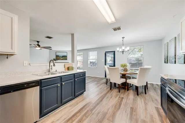 a large white dining hall with stainless steel appliances granite countertop a sink dishwasher a dining table and chairs with wooden floor