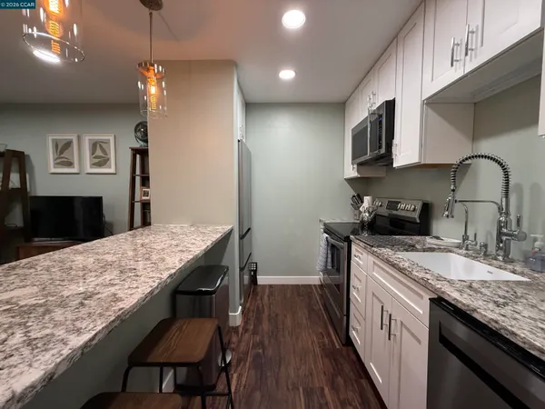 a kitchen with stainless steel appliances granite countertop wooden cabinets a stove top oven a sink dishwasher and a dining table with wooden floor