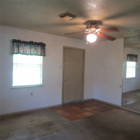 an empty room that has a chandelier fan and a window