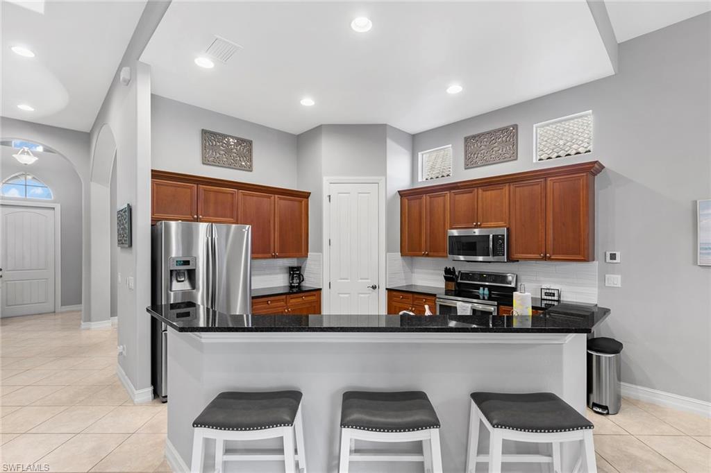 7778 Ashton Road Naples, FL 34113 - Photo 7 of 26 a kitchen with stainless steel appliances a refrigerator a stove a sink a dining table and chairs cabinets