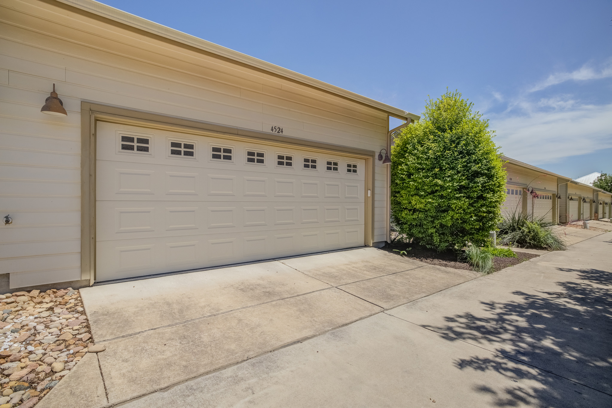 4524 Berkman Drive Austin, TX 78723 - Photo 37 of 38 Spacious garage with a paneled door featuring multiple window inserts, accompanied by concrete driveway paving, a decorative rock bed, and an exterior wall light fixture