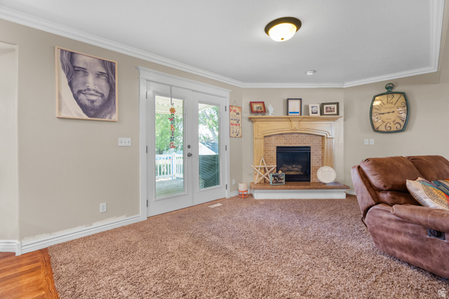 5727 South 3550th Street West Roy, UT 84067 - Photo 18 of 49 Living space featuring a corner fireplace with a brick surround and wood mantel, white crown molding, and double glass-paneled doors opening to an outdoor area