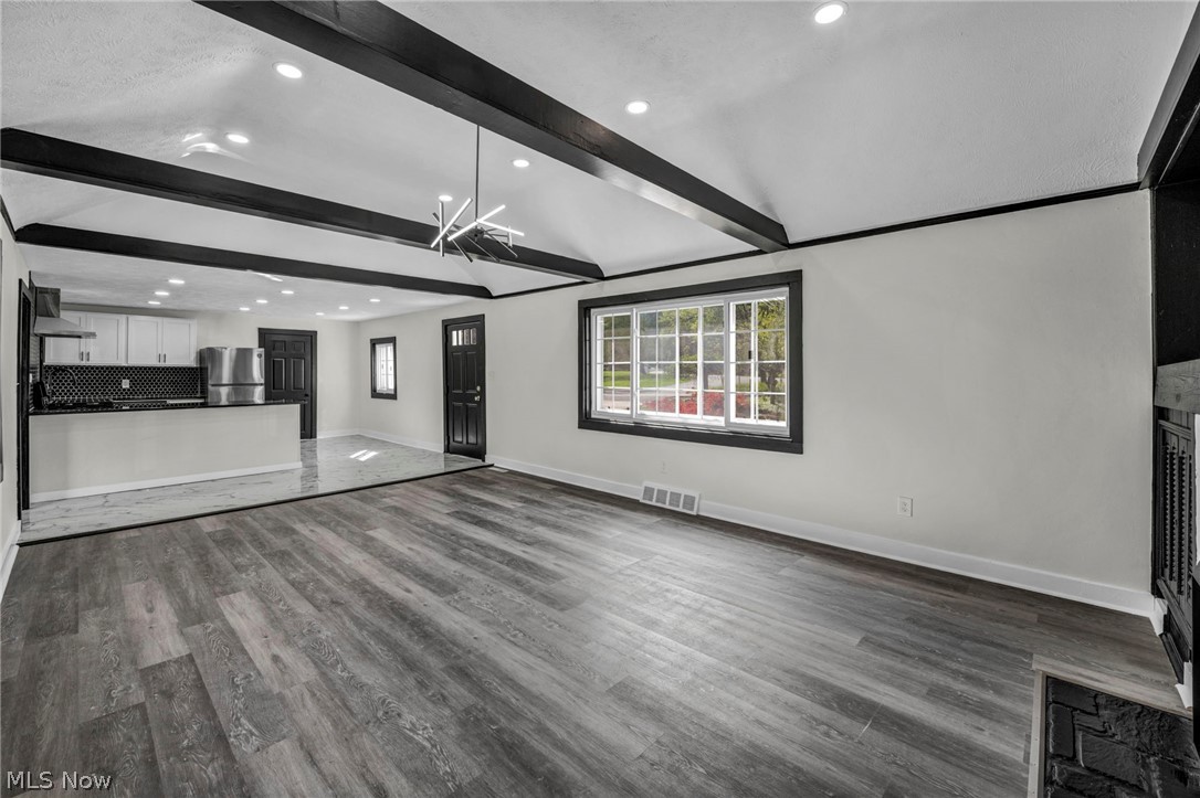 7339 River Road Olmsted Falls, OH 44138 - Photo 8 of 45 Spacious interior featuring wood-finish flooring, a kitchen with white cabinetry and black countertops, exposed ceiling beams, recessed lighting, and large windows
