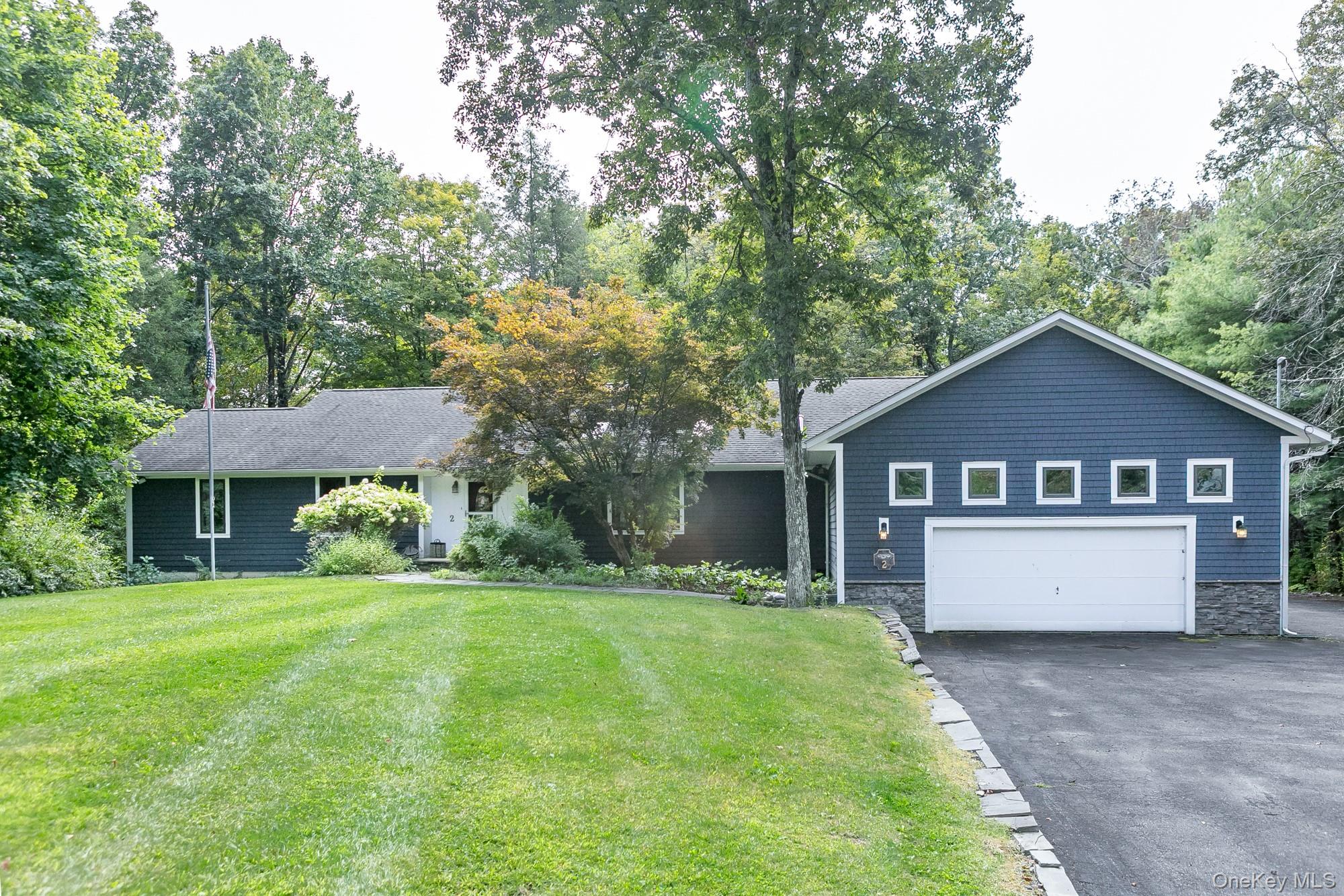 a house that is sitting in the grass with large trees and plants