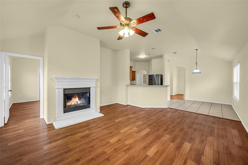 705 Loftin Street Crowley, TX 76036 - Photo 7 of 31 Unfurnished living room featuring vaulted ceiling, a ceiling fan, light wood finished floors, a glass covered fireplace, and arched walkways