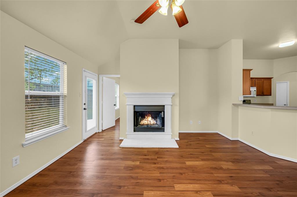 705 Loftin Street Crowley, TX 76036 - Photo 10 of 31 Unfurnished living room featuring a ceiling fan, dark wood finished floors, a lit fireplace, and lofted ceiling