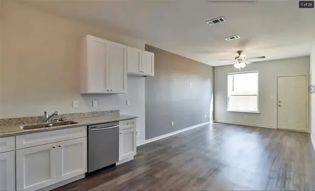 a kitchen with granite countertop a stove a sink and white cabinets with wooden floor