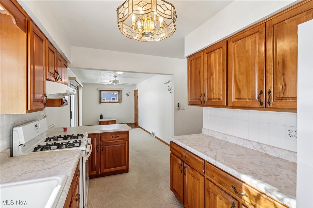 970 Eastern Road Doylestown, OH 44230 - Photo 13 of 49 Kitchen featuring backsplash, gas range gas stove, brown cabinets, light colored carpet, and light countertops