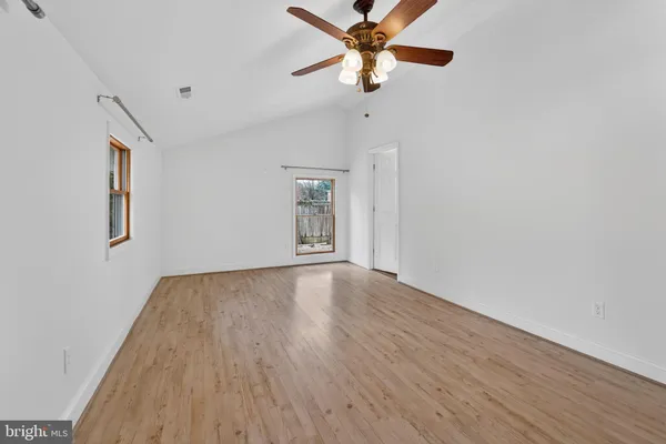 an empty room with wooden floor fan and windows
