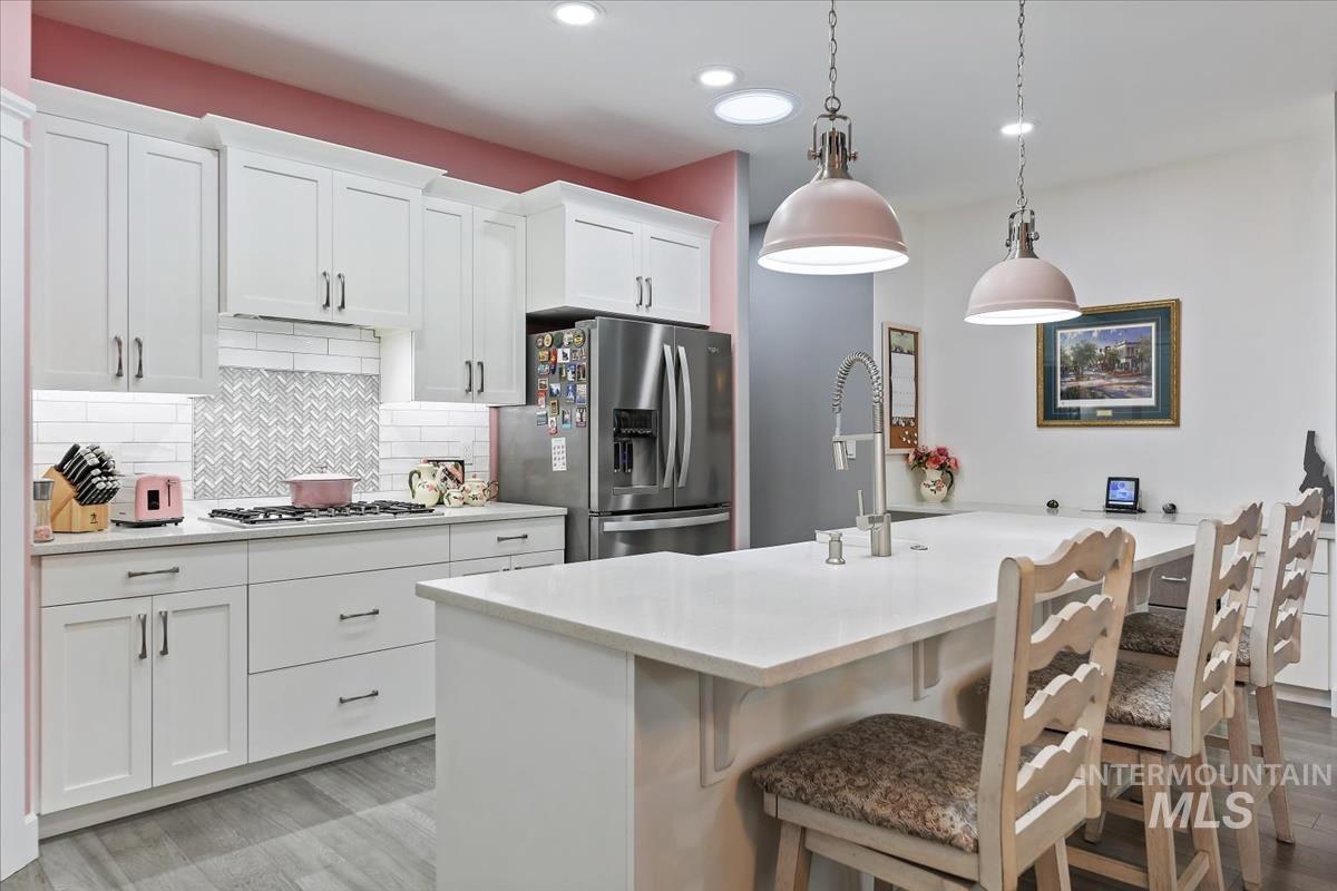 189 South Devon Avenue Star, ID 83669 - Photo 6 of 42 Kitchen featuring stainless steel refrigerator with ice dispenser, a kitchen bar, white cabinets, decorative light fixtures, and decorative backsplash