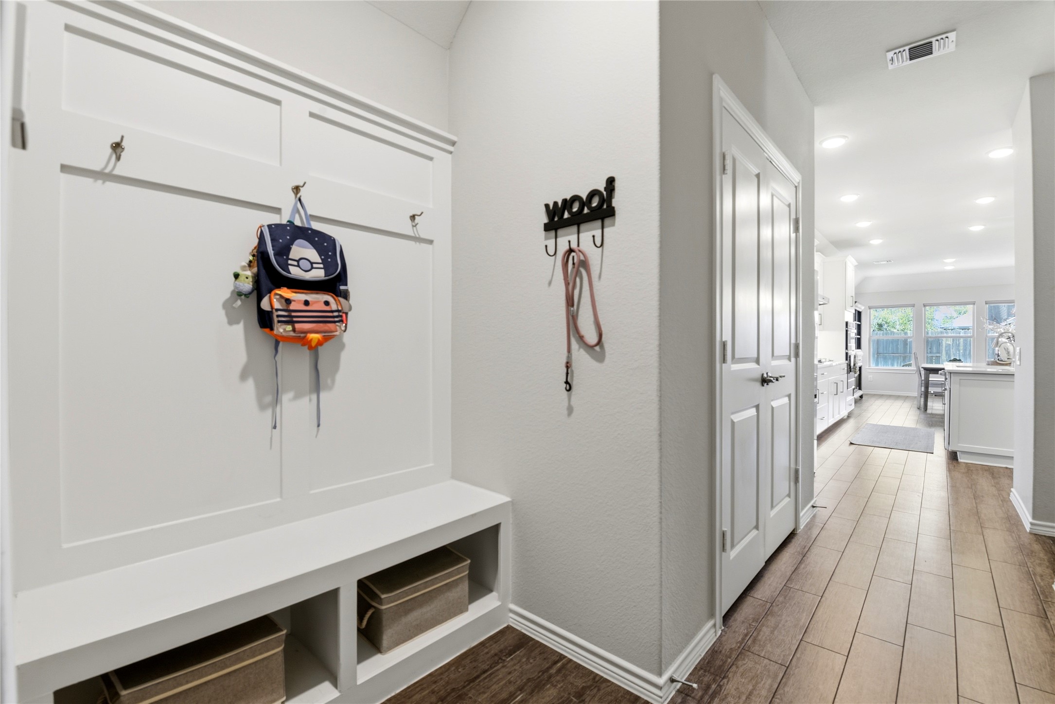 17834 Maple Ash Drive Spring, TX 77379 - Photo 19 of 50 This photo shows a bright and welcoming entryway from garage with built-in storage benches and hooks for organization. The hallway features wood-look flooring, leading to an open kitchen with large windows that provide plenty of natural light.