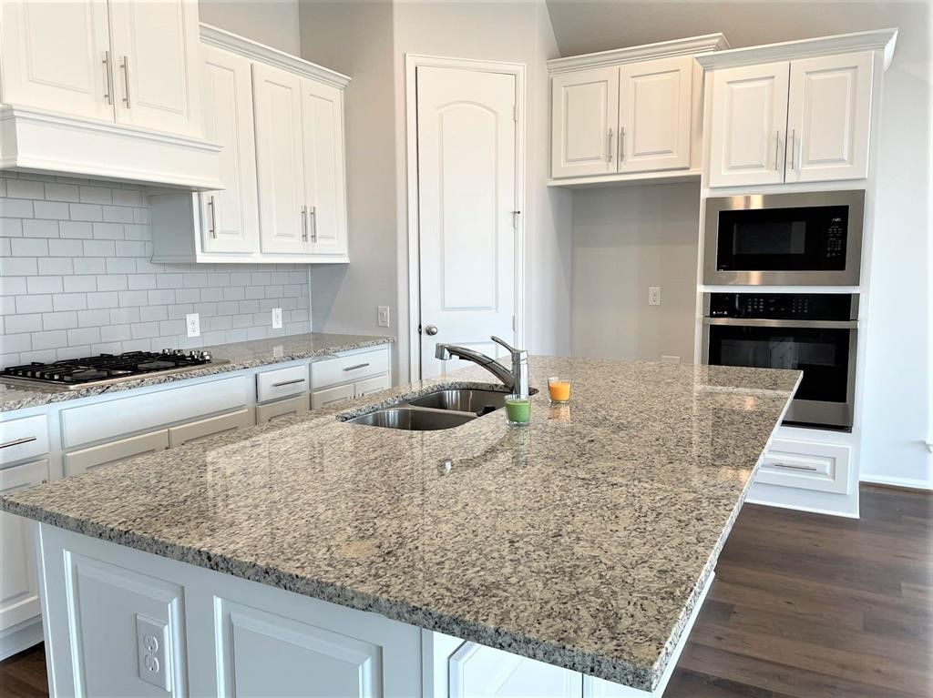 156 Santa Maria Street Georgetown, TX 78628 - Photo 13 of 40 Kitchen with dark wood-type flooring, white cabinets, light stone countertops, stainless steel appliances, and a center island with sink