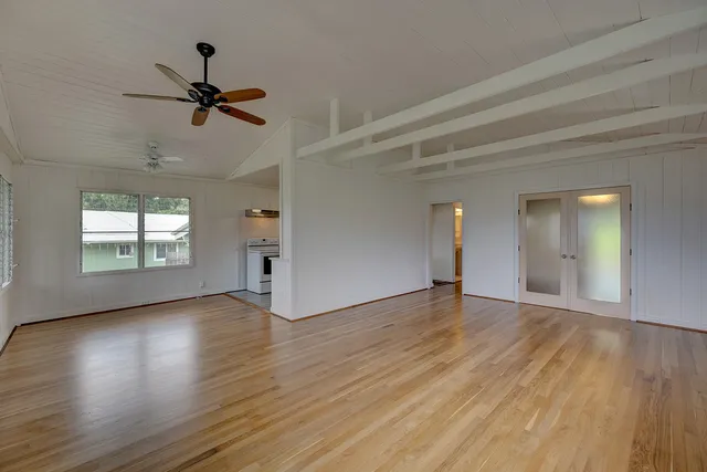 an empty room with wooden floor a ceiling fan and windows
