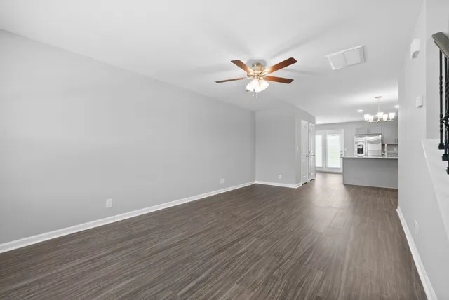 an empty room with wooden floor and a kitchen view