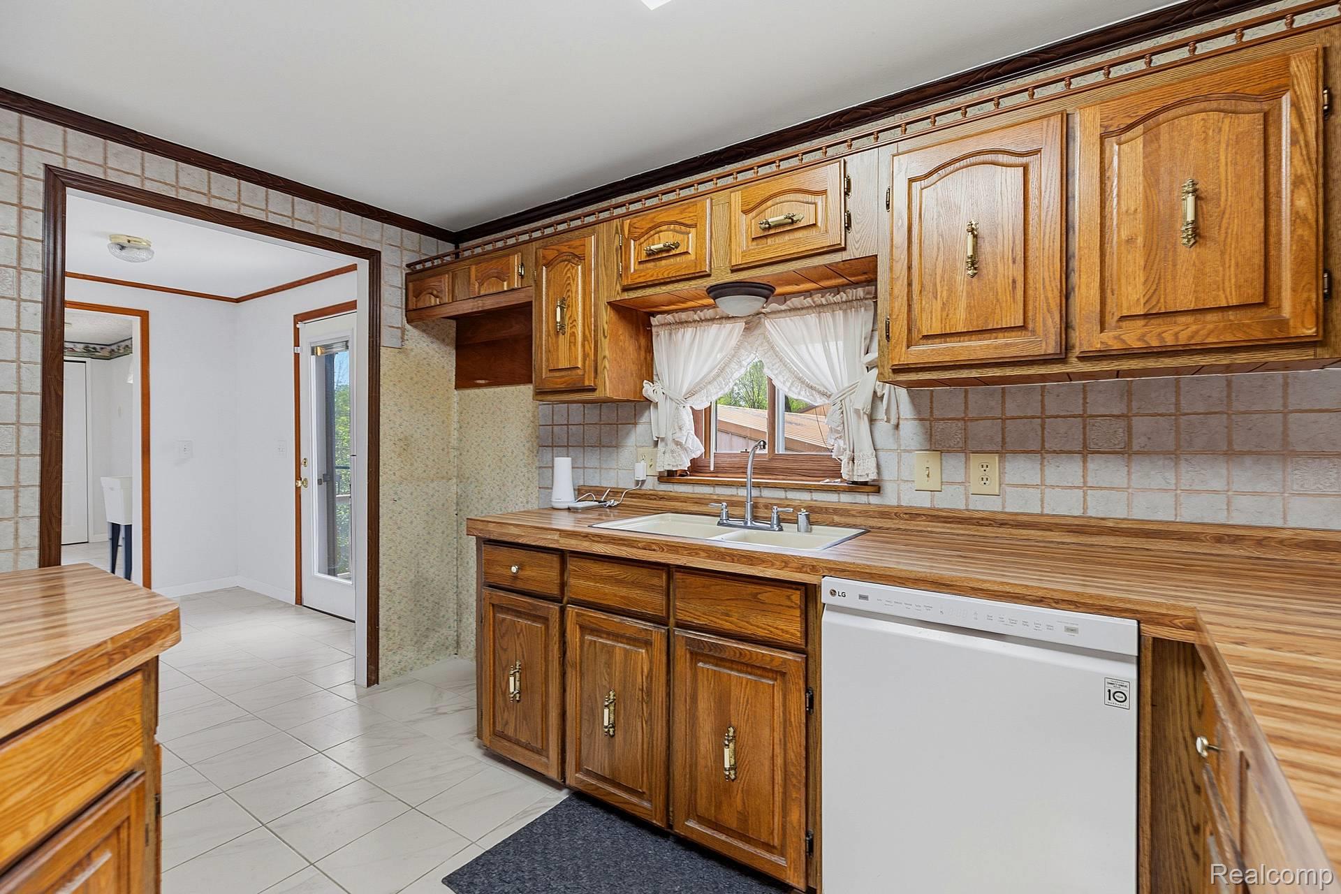 70919 Coon Creek Road Armada, MI 48005 - Photo 15 of 50 Kitchen featuring crown molding, wood finish cabinetry, white dishwasher, wallpapered walls, and decorative backsplash