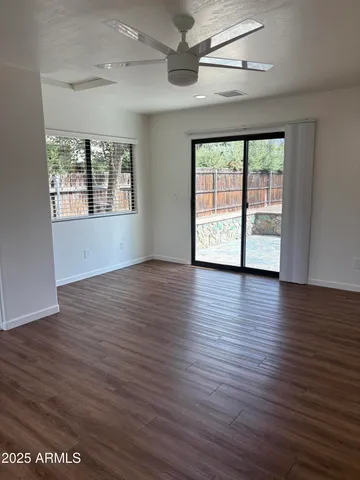 an empty room with wooden floor chandelier fan and windows