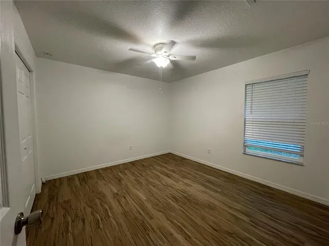 a view of an empty room with chandelier fan and wooden floor