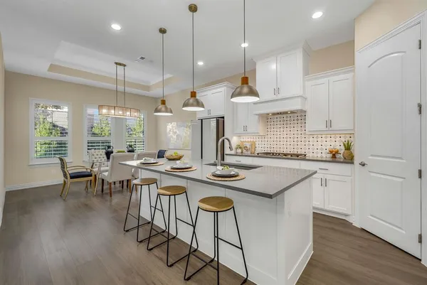 a kitchen with stainless steel appliances granite countertop a stove a refrigerator a kitchen island a dining table and chairs with wooden floor
