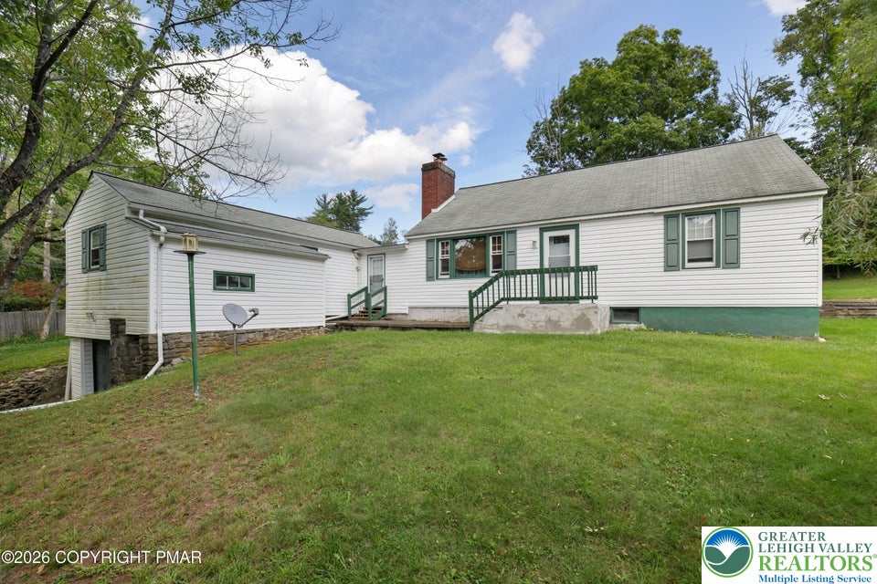 Mature trees frame a classic exterior featuring a grassy lawn and vinyl siding.