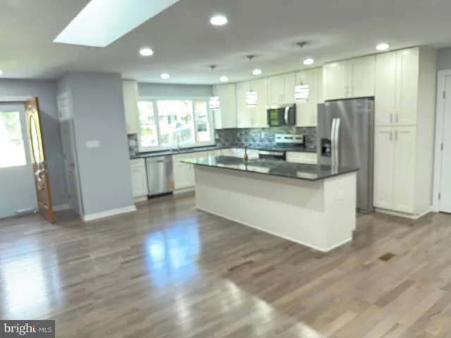 a large kitchen with kitchen island a sink a stove a refrigerator and white cabinets with wooden floor