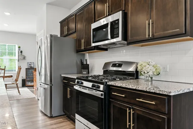 a kitchen with stainless steel appliances a stove a sink a microwave a refrigerator a dining table and chairs with wooden floor