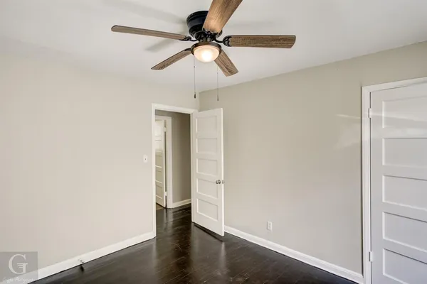 an empty room with wooden floor fan and windows