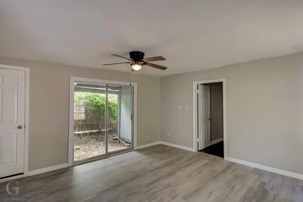 a view of an empty room with wooden floor and fan