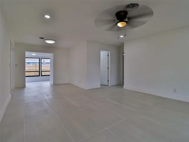 an empty room with chandelier fan and windows
