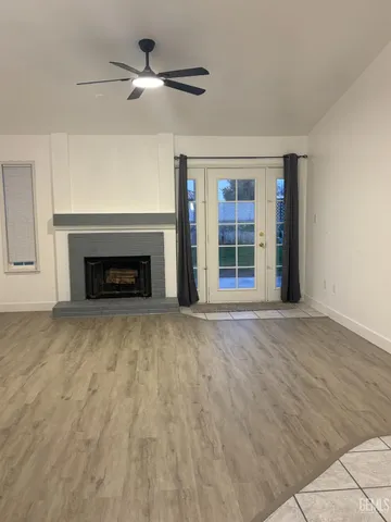 a view of an empty room with wooden floor fireplace and a window