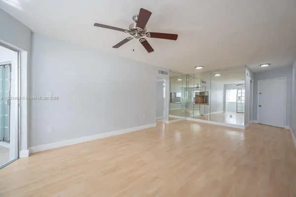 a view of an empty room with wooden floor and a ceiling fan