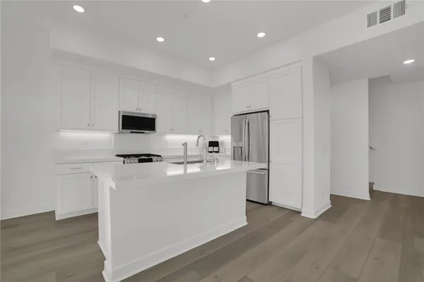 a kitchen with stainless steel appliances a sink dishwasher stove refrigerator and white cabinets with wooden floor