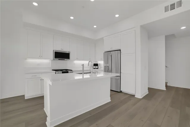 a kitchen with stainless steel appliances a sink dishwasher stove refrigerator and white cabinets with wooden floor