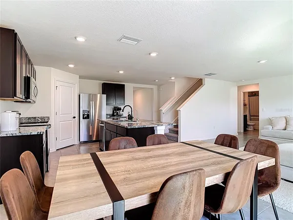 a kitchen with stainless steel appliances kitchen island granite countertop a dining table chairs sink and cabinets