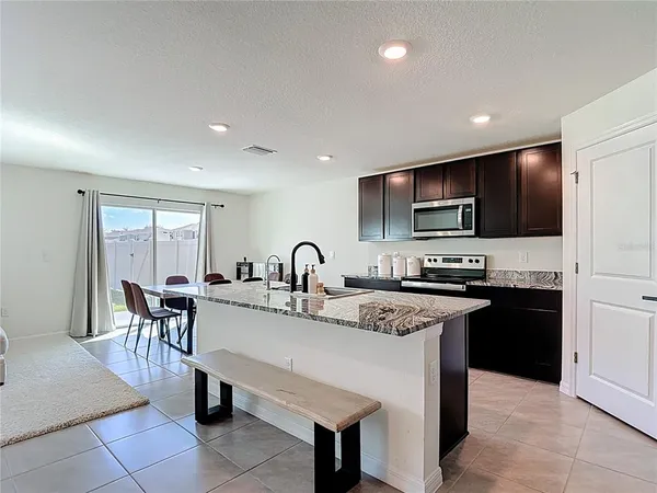 a kitchen with stainless steel appliances granite countertop a stove top oven a sink dishwasher a dining table and chairs with wooden floor