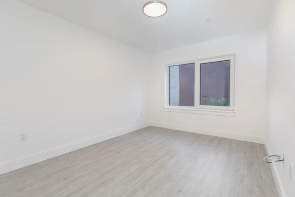 a view of an empty room with wooden floor and fan