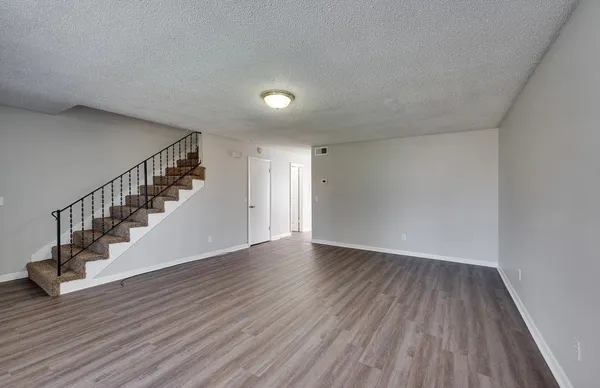 a view of an empty room with wooden floor and stairs