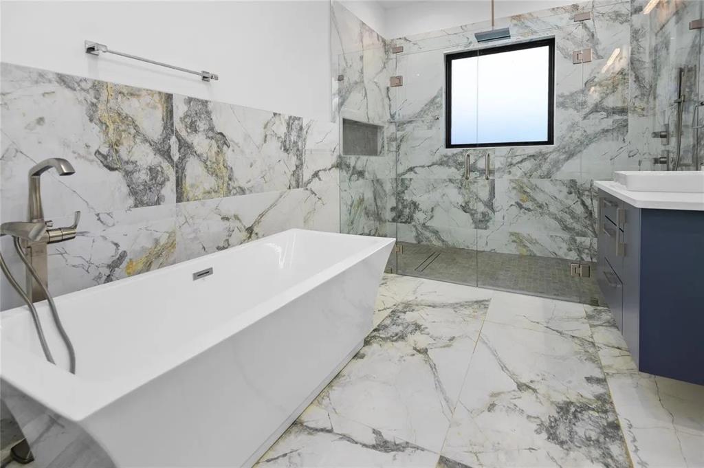309 Kaye Street Coppell, TX 75019 - Photo 22 of 36 Freestanding soaking tub with a floor-mounted brushed nickel faucet, large format marble-look tile flooring and shower surround, and a glass-enclosed shower with a built-in niche
