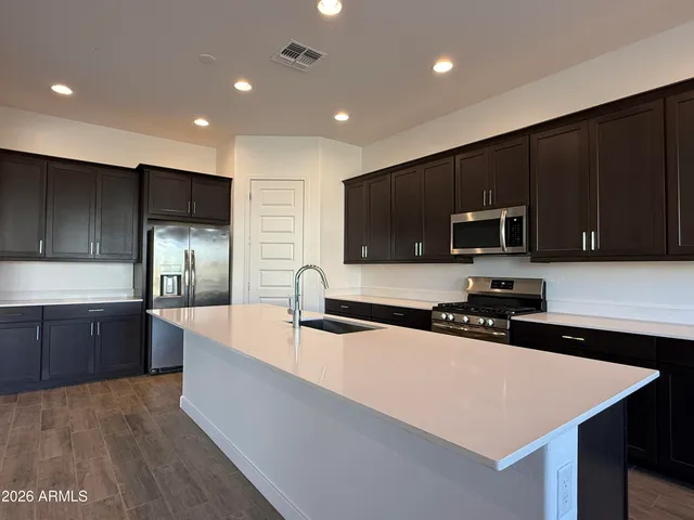 a large kitchen with stainless steel appliances a sink a stove a microwave a refrigerator a center island and wooden cabinets