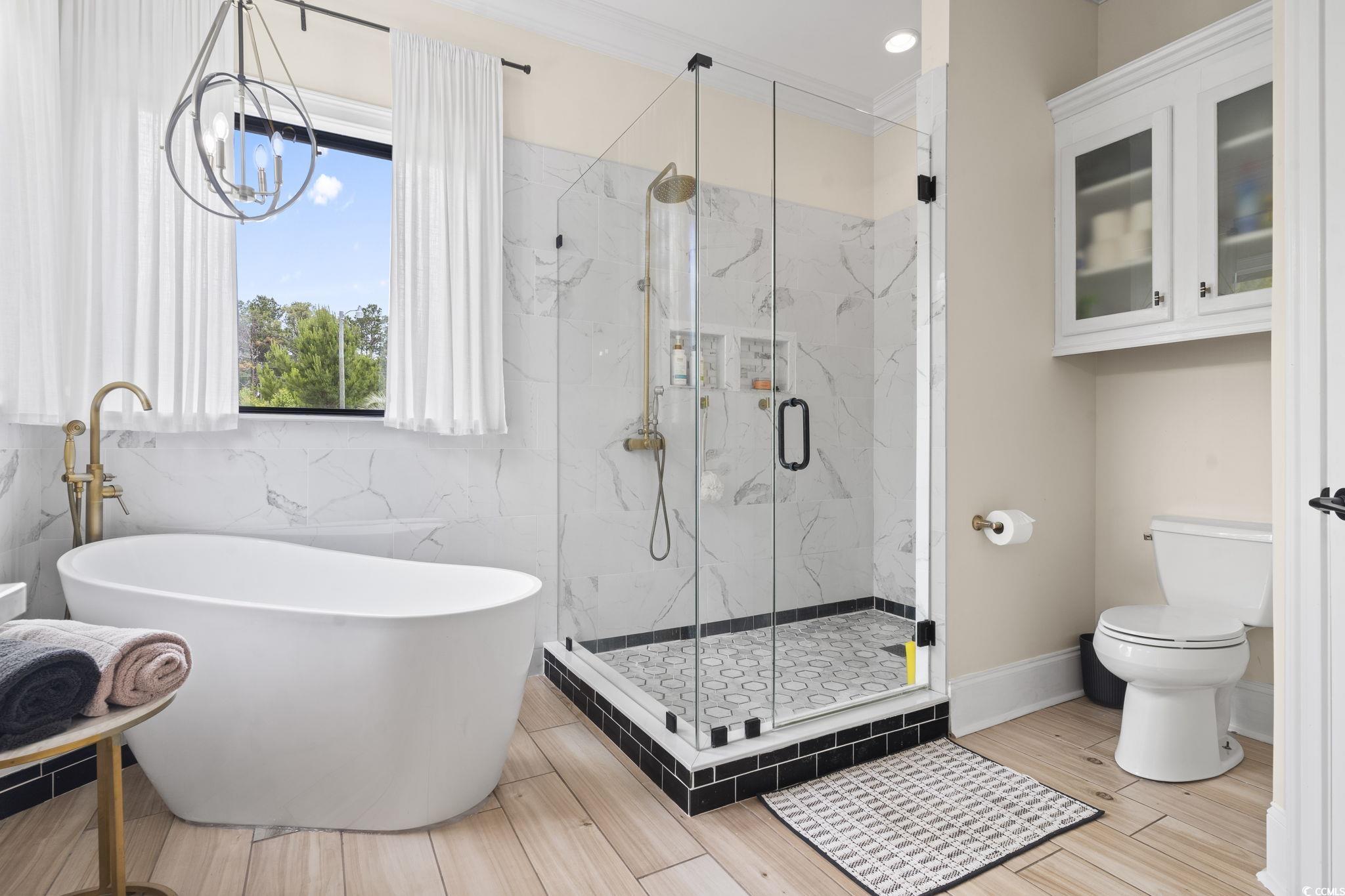 9449 Freewoods Road Myrtle Beach, SC 29588 - Photo 19 of 39 Bathroom featuring toilet, a freestanding tub, a marble finish shower, tile walls, and a chandelier