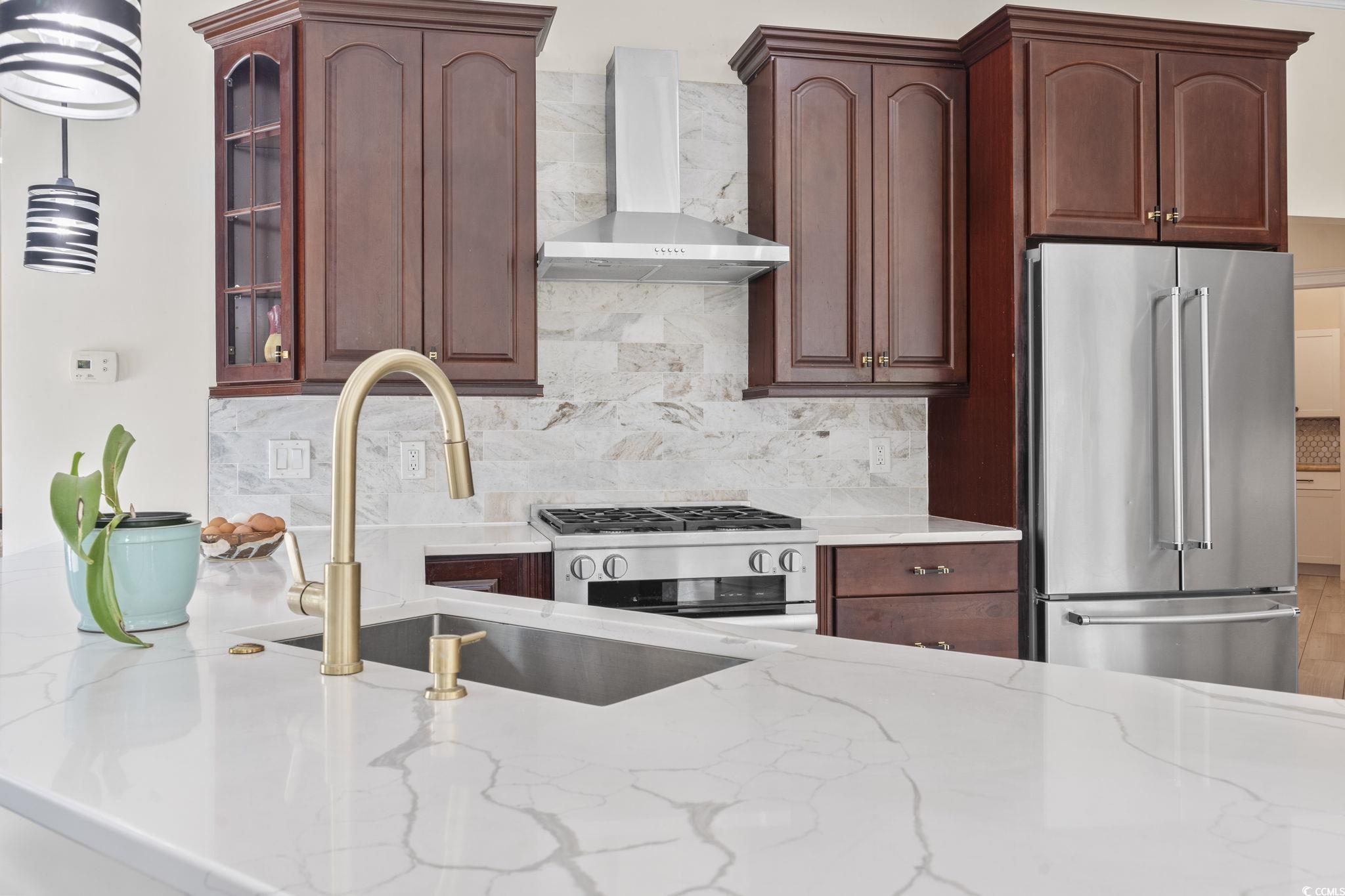 9449 Freewoods Road Myrtle Beach, SC 29588 - Photo 7 of 39 Kitchen with appliances with stainless steel finishes, wall chimney range hood, a sink, light stone countertops, and backsplash