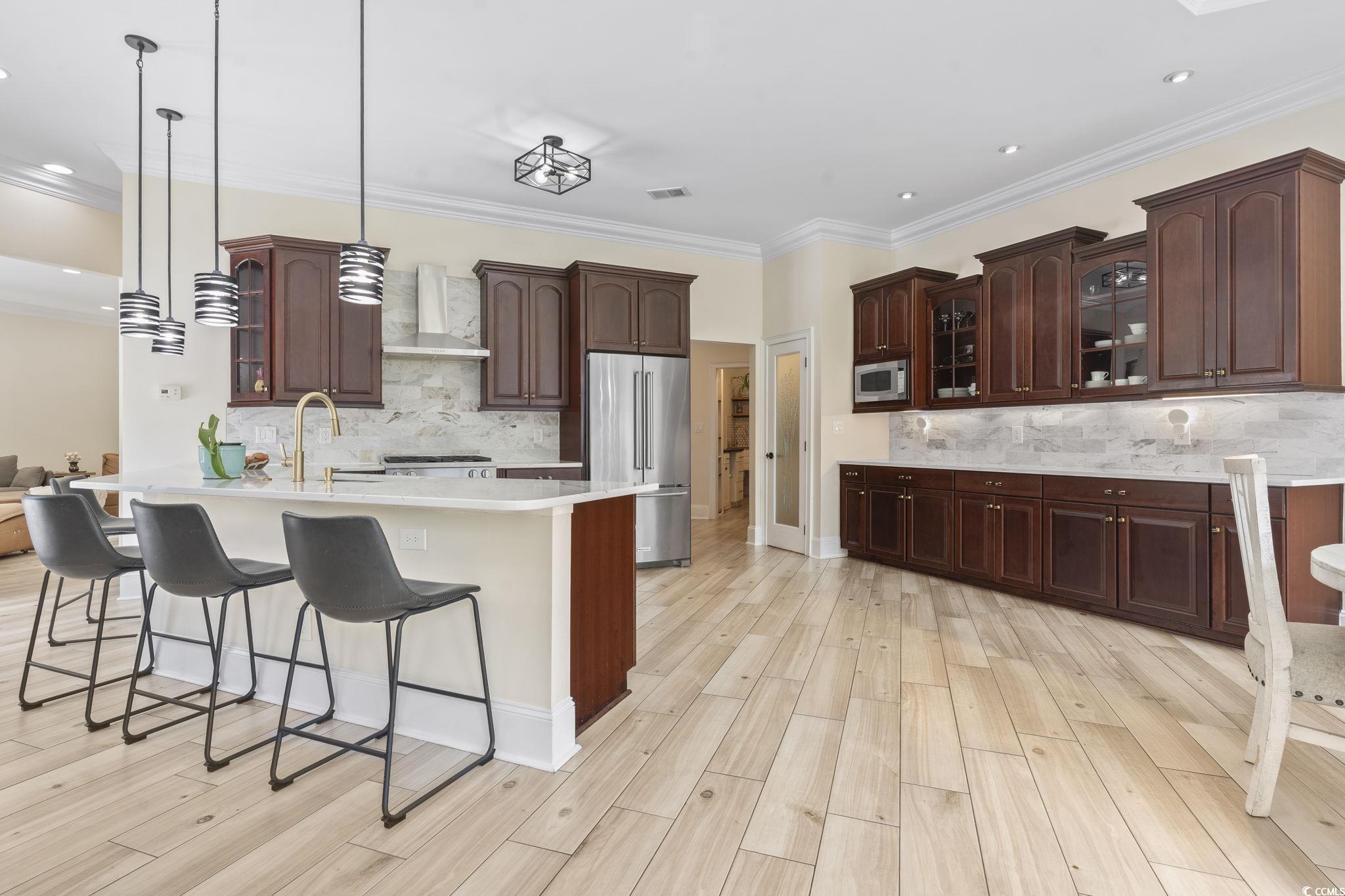 9449 Freewoods Road Myrtle Beach, SC 29588 - Photo 10 of 39 Kitchen featuring appliances with stainless steel finishes, wall chimney exhaust hood, a kitchen breakfast bar, light countertops, and tasteful backsplash