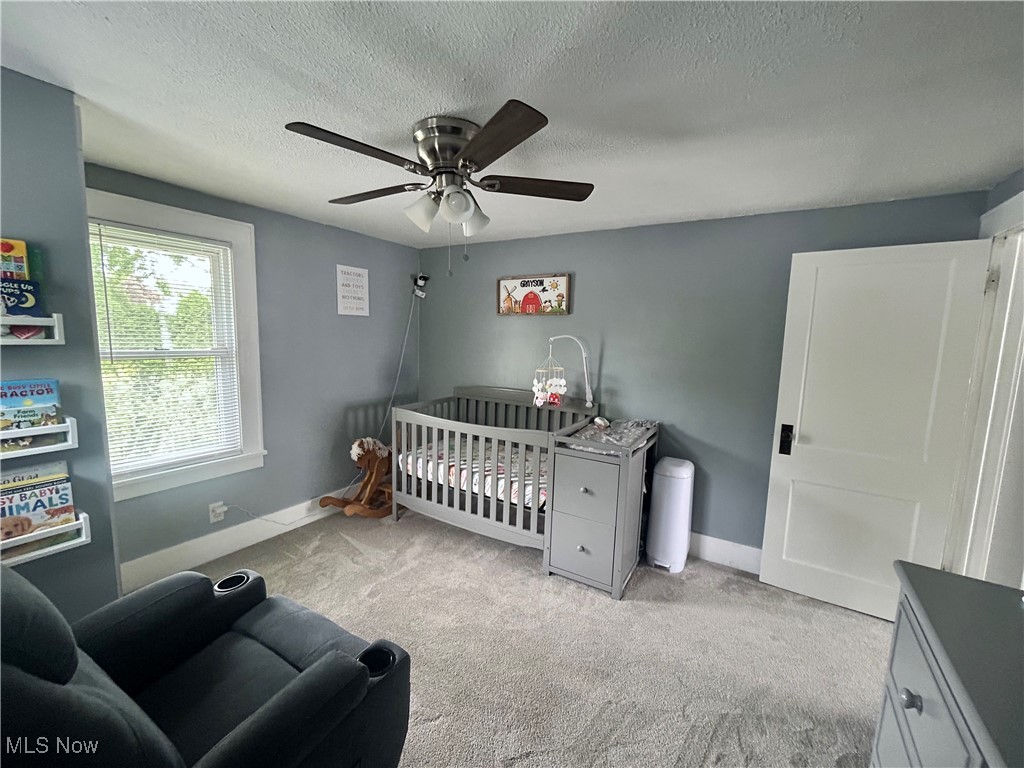 935 Lilly Road Alliance, OH 44601 - Photo 27 of 31 Carpeted bedroom featuring a crib, a textured ceiling, baseboards, and ceiling fan