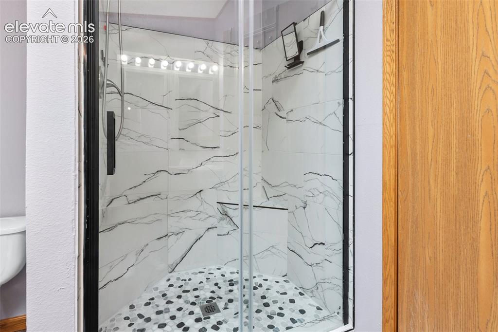 1350 South Calhan Highway Yoder, CO 80864 - Photo 32 of 45 Walk-in shower featuring clear glass enclosure with dark trim, marble-patterned wall tiles, and a pebble-style floor