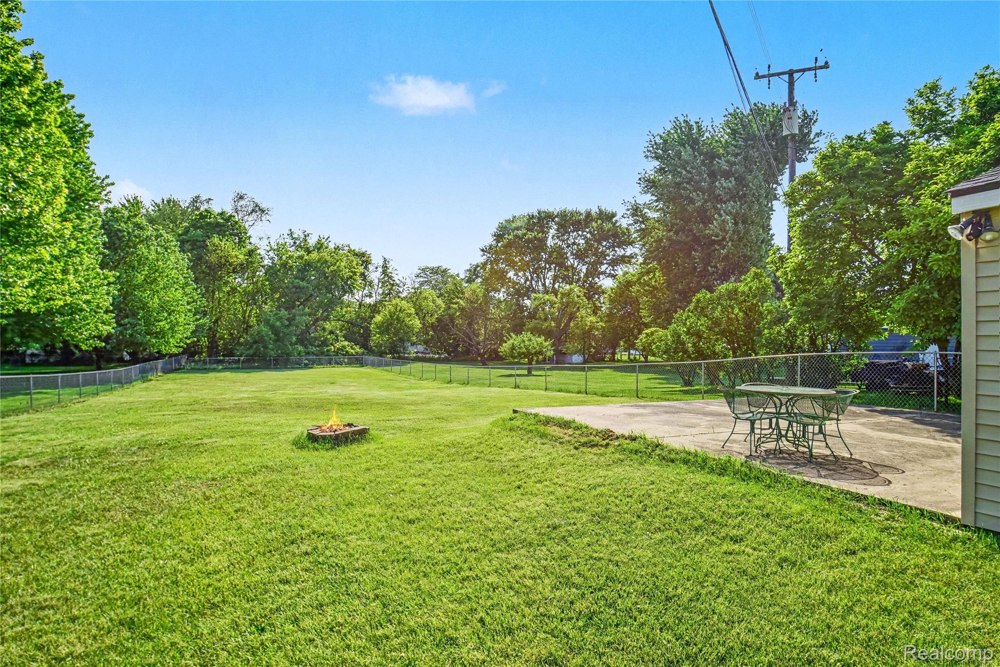 8530 Canal Road Sterling Heights, MI 48314 - Photo 24 of 31 Spacious backyard featuring a large grass lawn, chain-link fencing, a stone fire pit, and a concrete patio