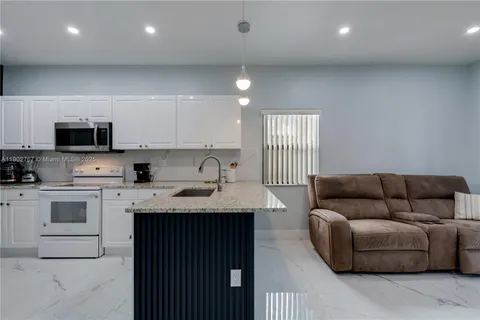 a living room with stainless steel appliances granite countertop couches a kitchen island a sink dishwasher and a stove with wooden floor