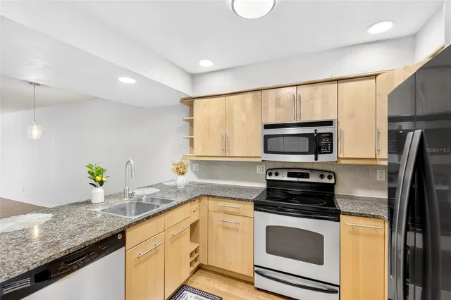 a kitchen with stainless steel appliances granite countertop a sink a stove a microwave a refrigerator a counter space and cabinets